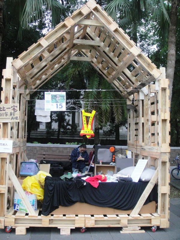 圖3之2：台大學生在校門口擺放一棟精巧的自製木頭模型屋，高達數公尺，稱為「家的真實再現」。王立柔/攝   
