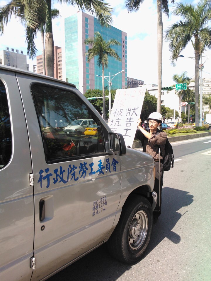抗議現場巧遇勞委會車輛，台灣國際勞工協會研究員吳永毅一馬當先，手持「被坑無感，壯告工人」手舉牌，將勞委會的公務車擋在。圖片來源：台灣國際勞工協會提供   