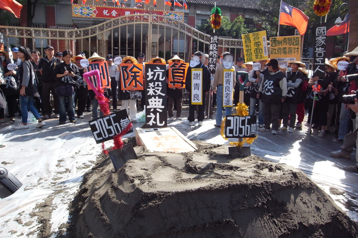 勞工團體在立法院門口堆起一卡車的土堆，埋住一個象徵勞工棺材本的棺材，上頭立起寫著「坑殺典禮」的立牌，浩浩蕩蕩舉辦動土典禮，諷刺政府容許謝青良坑殺勞保棺材本，卻編列千萬預算要向關廠工人提告。圖：楊宗興/攝   