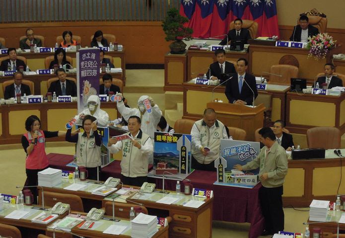 民進黨新北市議會黨團成員以穿防護衣、折斷核燃料棒模型的方式，宣示「根本沒有真正的核安，所以不能有核能」的理念。圖：陳冠廷/攝   