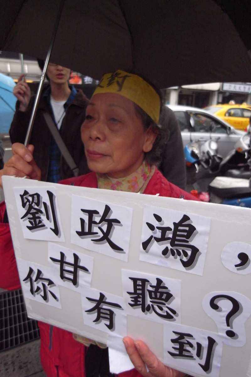 苗栗灣寶社區居民反對後龍科技園區徵收土地，一位老婦人手持「劉政鴻，你甘有聽到？」標語，在大雨中站在營建署前表達反對立場。圖片：楊宗興/攝   